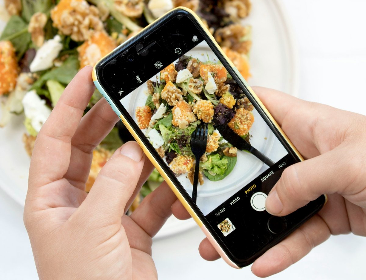 Bild zeigt wie jemand mit dem Smartphone seine Mahlzeit fotografiert. Zu sehen ist nur die Hand und der Bildschirm  auf dem Smartphone.
